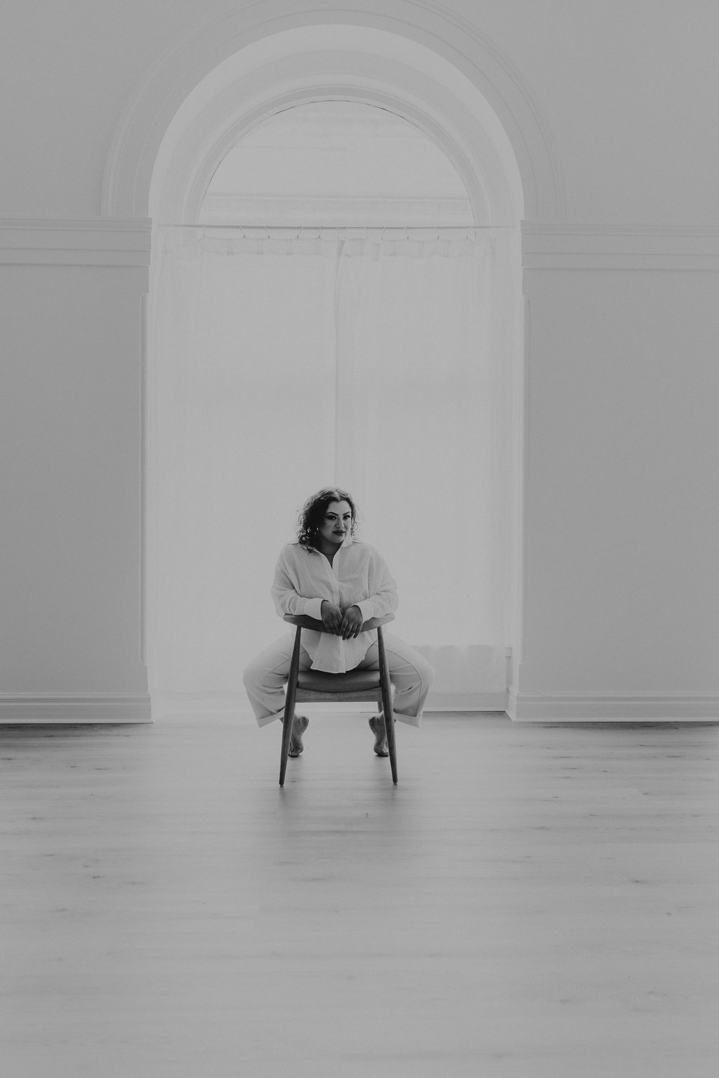 Char, full-length portrait seated under an arched window at Chars Lash Bar