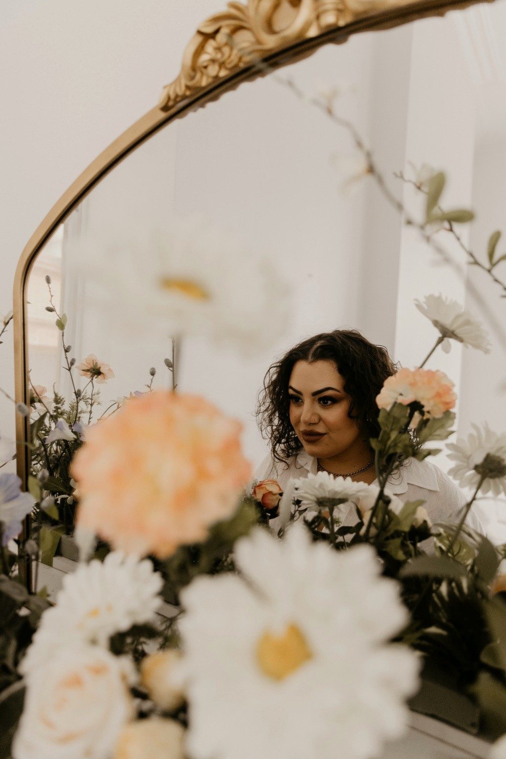 Char reflected in a gold arched mirror surrounded by flowers